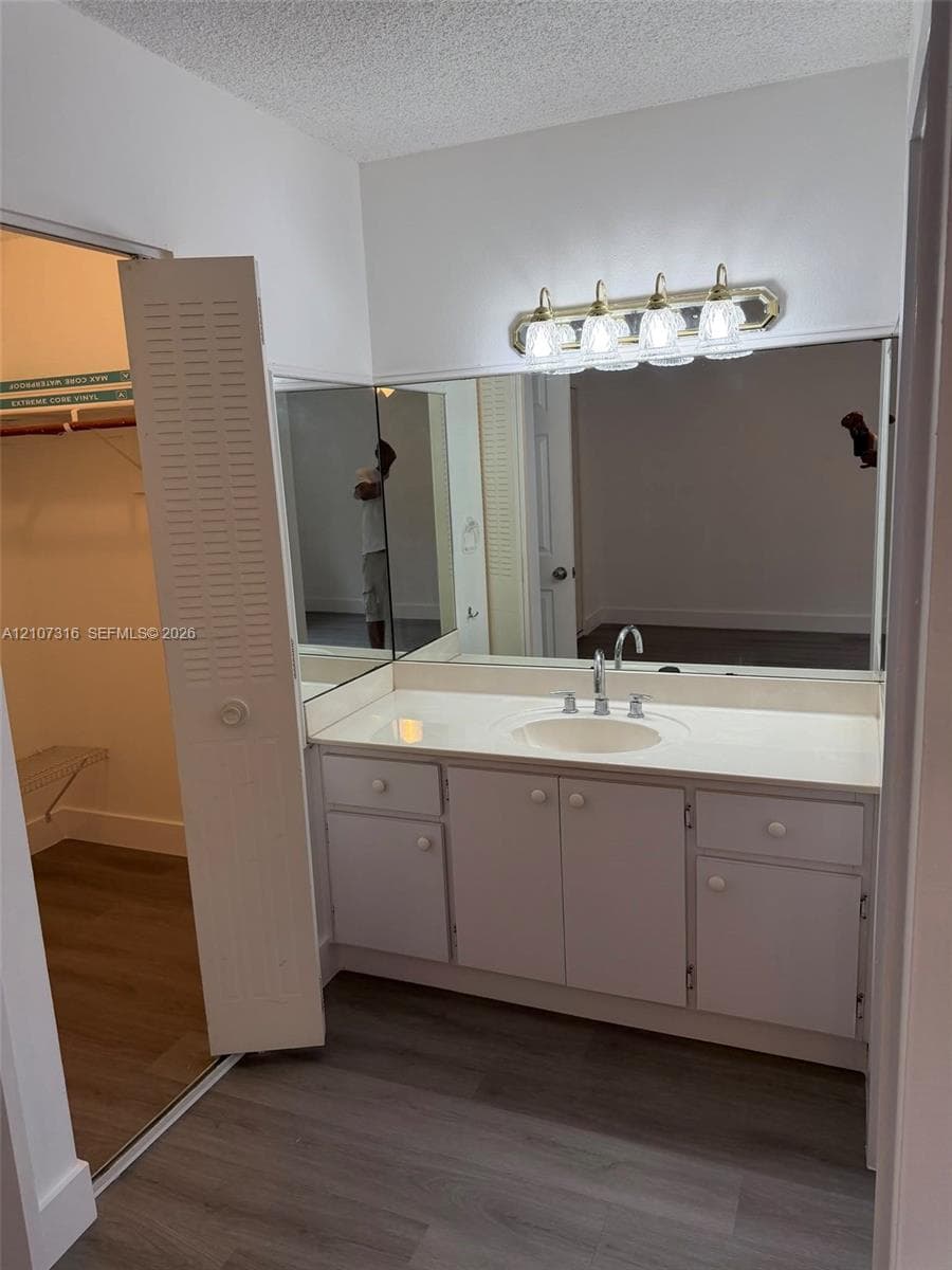 Vanity featuring a white countertop with an integrated oval basin, white cabinetry, a full-width wall mirror, and a four-bulb light fixture