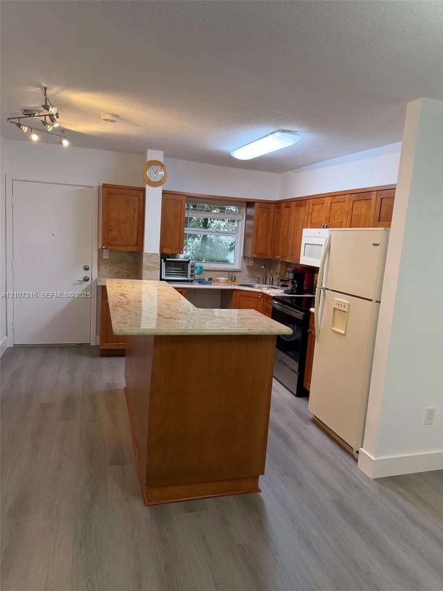 Kitchen featuring wood cabinetry, stone-surface breakfast bar, wood-finish flooring, and recessed track lighting