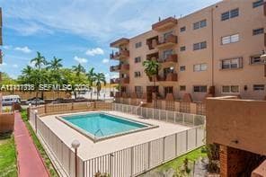 Multi-story residential building featuring private balconies, integrated swimming pool, metal security fencing, and palm tree landscaping