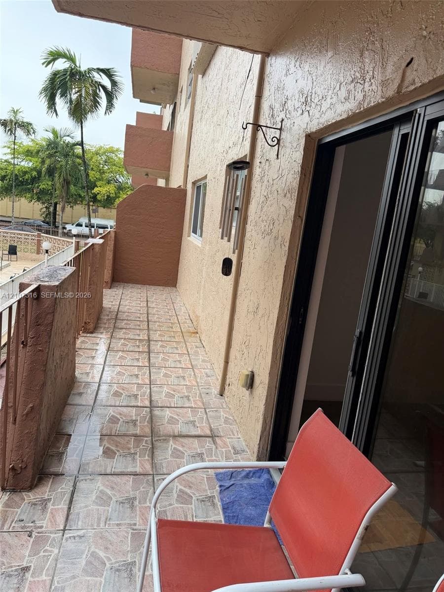 Covered balcony featuring patterned tile flooring, a metal railing, and a sliding glass door entrance