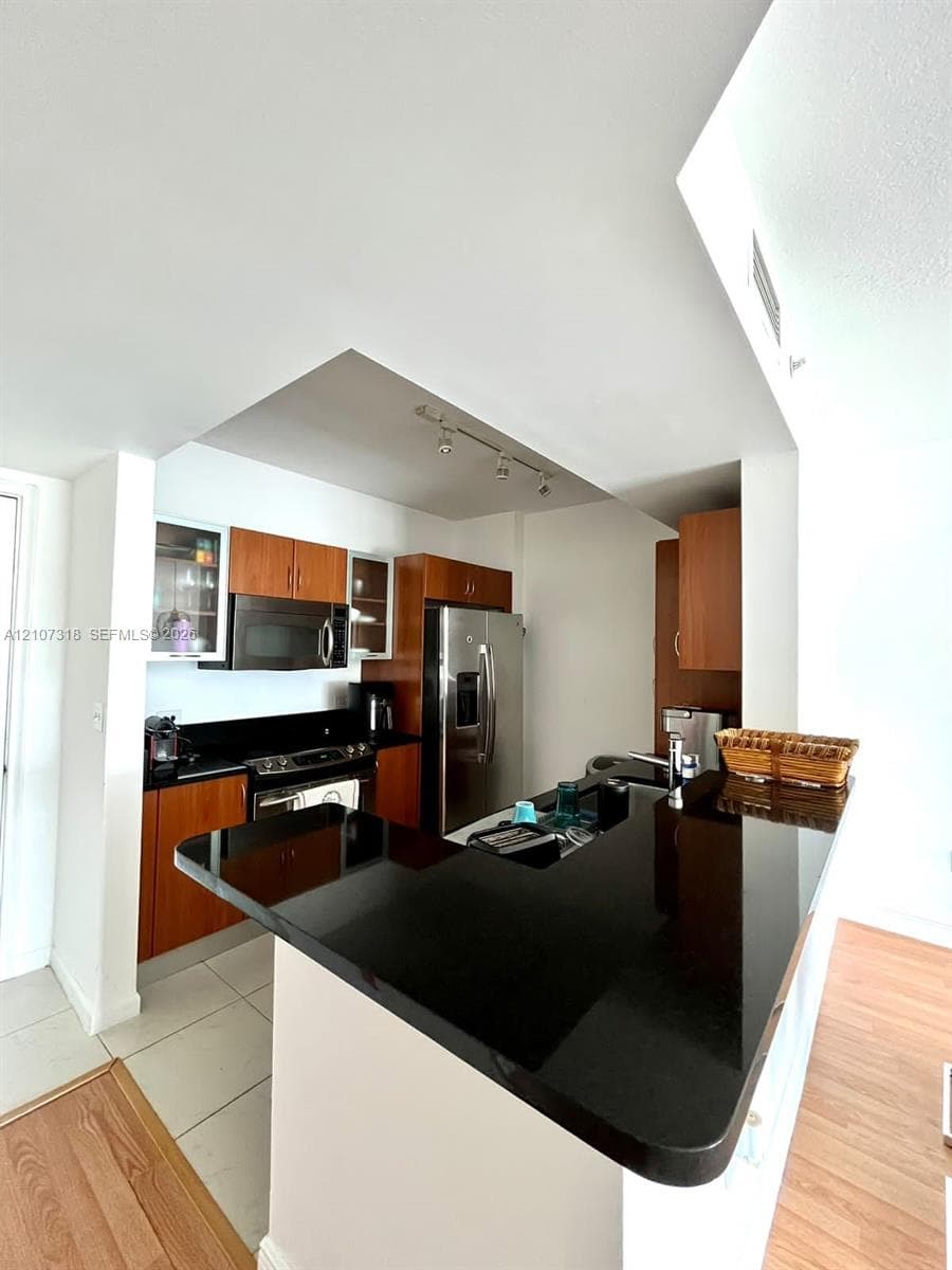 Kitchen featuring wood cabinetry, black solid-surface countertops, stainless steel appliances, and a breakfast bar
