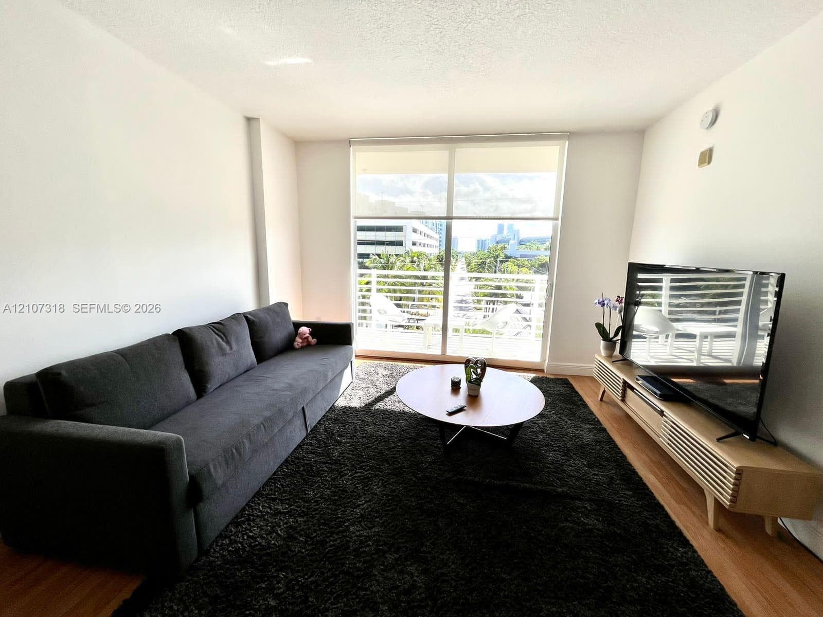 Living area featuring floor-to-ceiling glass sliding doors, wood-finish flooring, and an attached balcony with railing