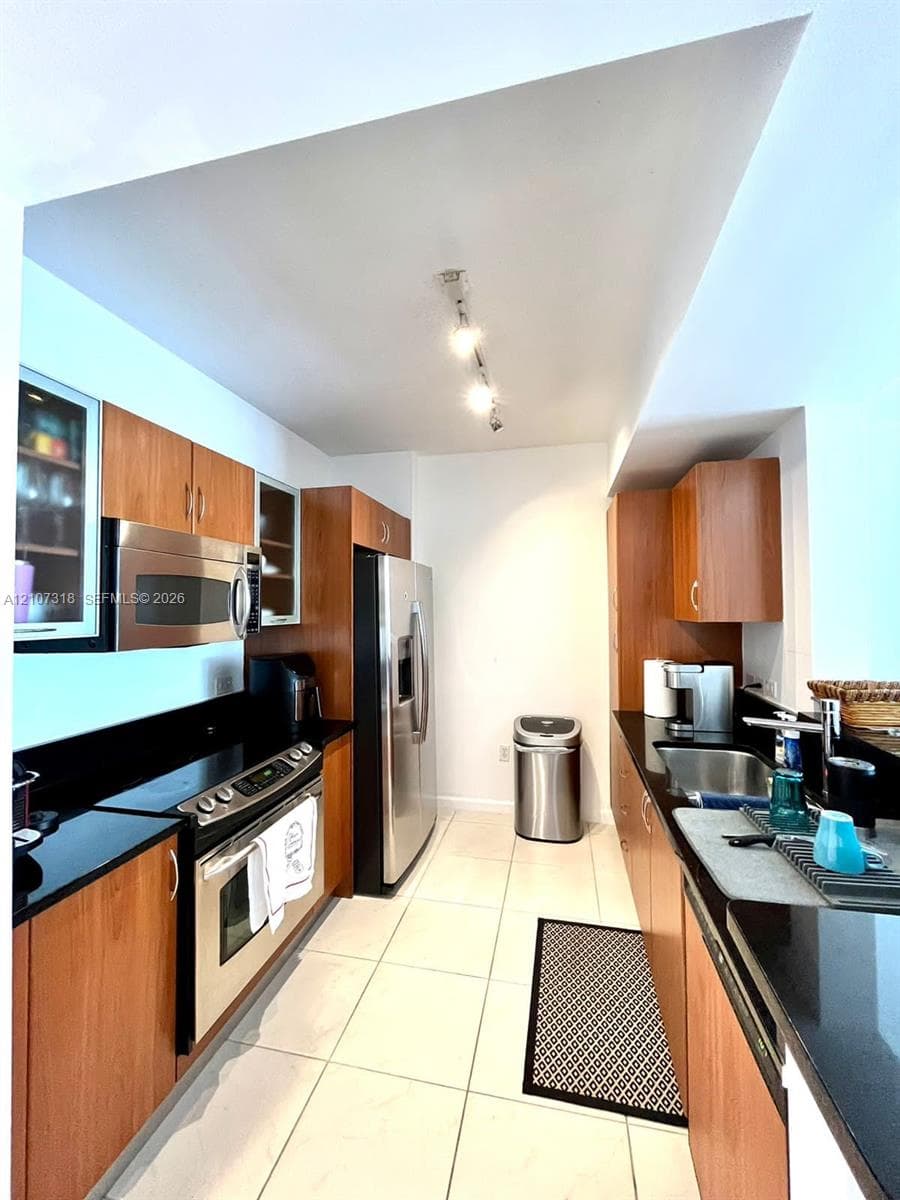 Kitchen featuring wood-finish cabinetry, solid surface countertops, stainless steel appliances, and large-format tile flooring