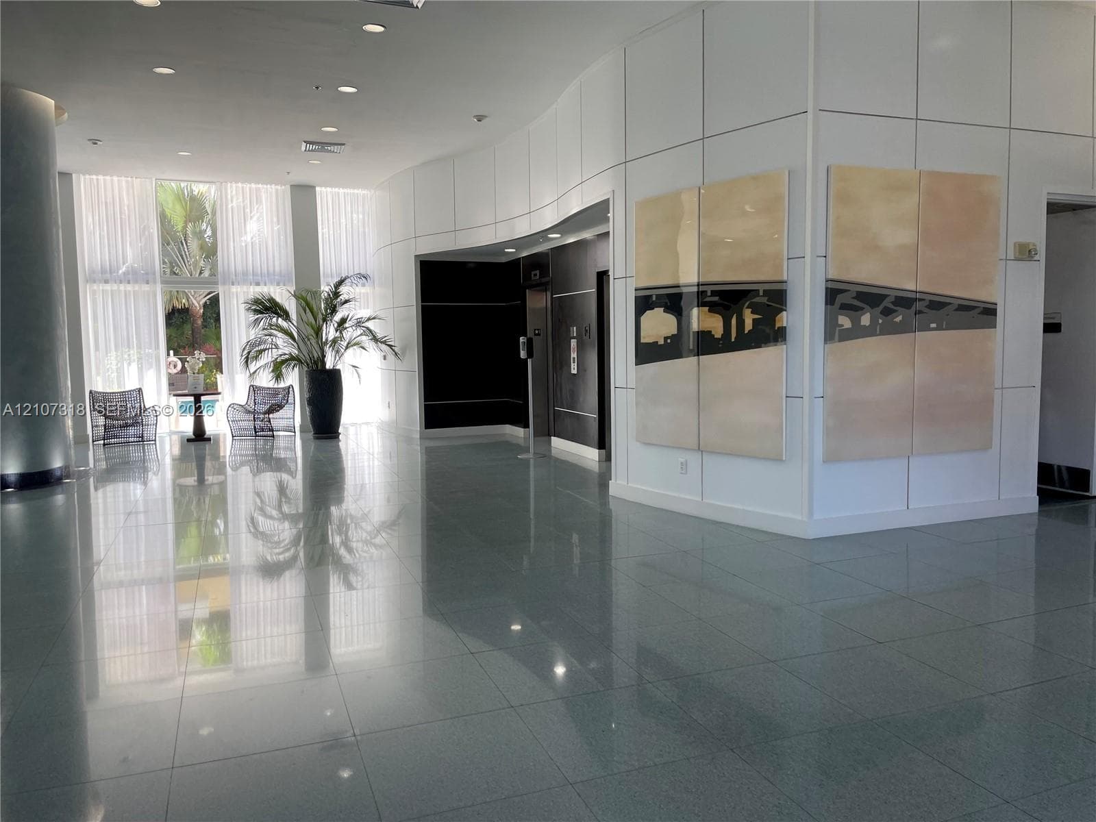 Modern lobby featuring floor-to-ceiling windows, polished stone flooring, recessed ceiling lighting, and a curved architectural wall panel system