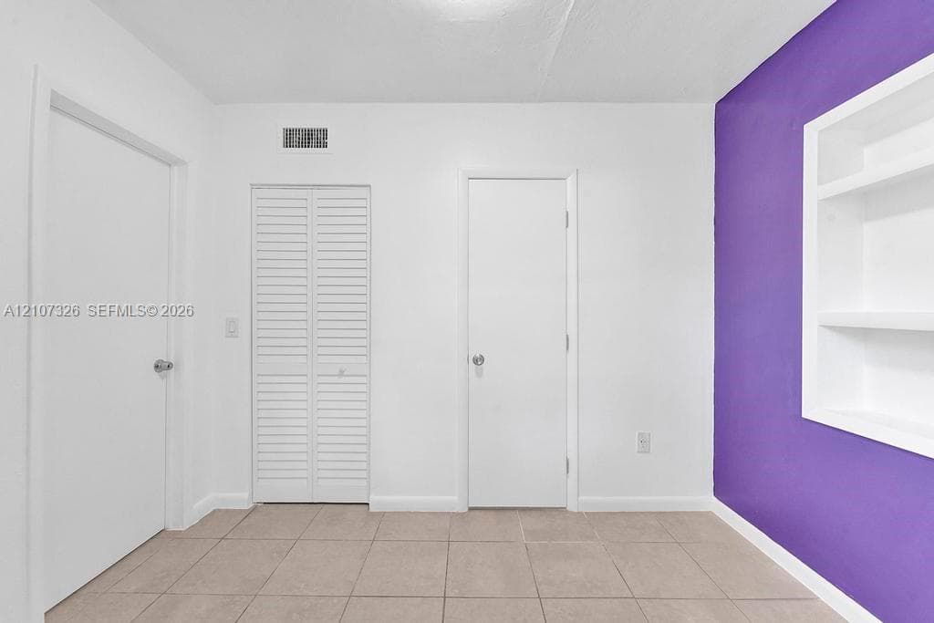 Neutral-toned tile flooring, built-in shelving unit, and louvered closet doors
