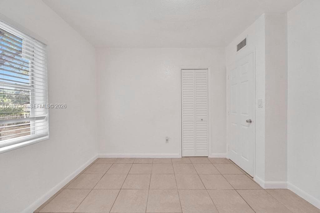 Neutral-toned tile flooring, white interior walls, white paneled door, louvered-style closet door, and window with horizontal blinds