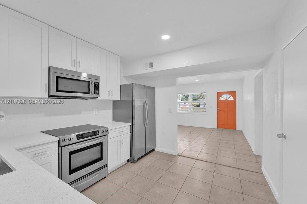 Kitchen featuring white cabinetry, solid-surface countertops, and stainless steel appliances including a built-in microwave, range, and refrigerator