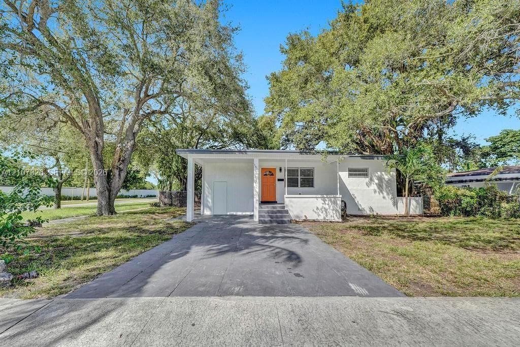 Single-story exterior featuring white stucco siding, a covered front entryway, concrete driveway, and mature landscaping