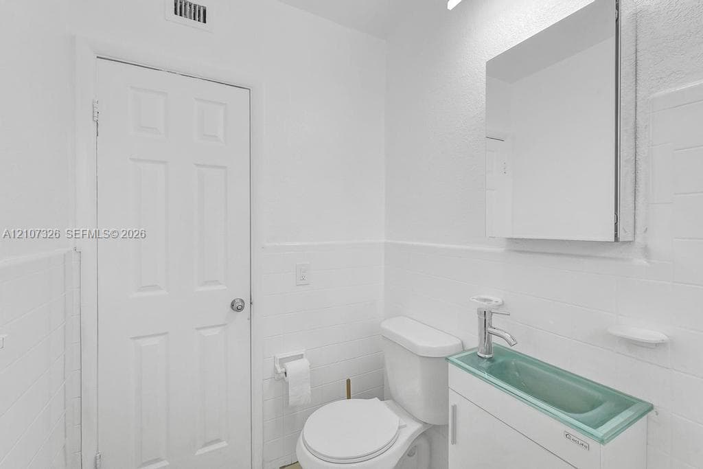 Bathroom featuring white tile wall cladding, a floating vanity with a glass basin and integrated faucet, and a wall-mounted mirrored medicine cabinet