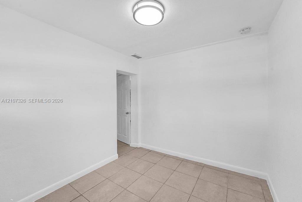 Interior room featuring neutral ceramic tile flooring, crisp white walls, and a circular flush-mount ceiling light fixture