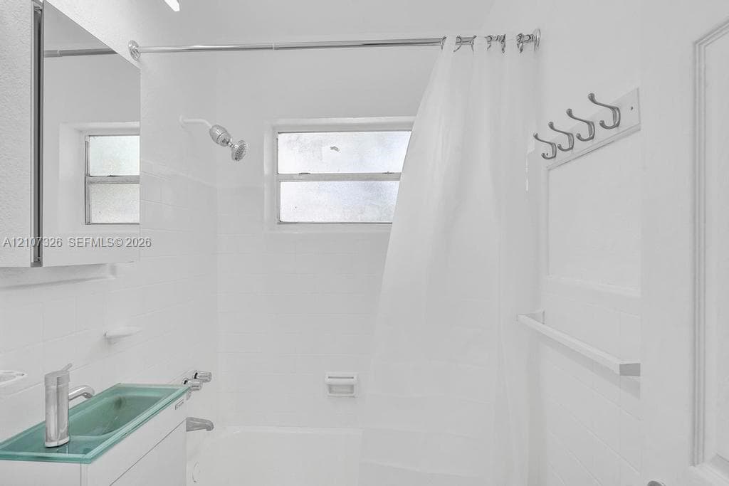 Bathroom featuring a glass vessel sink, chrome fixtures, a combination tub and shower with tile surround, and a wall-mounted hook rack