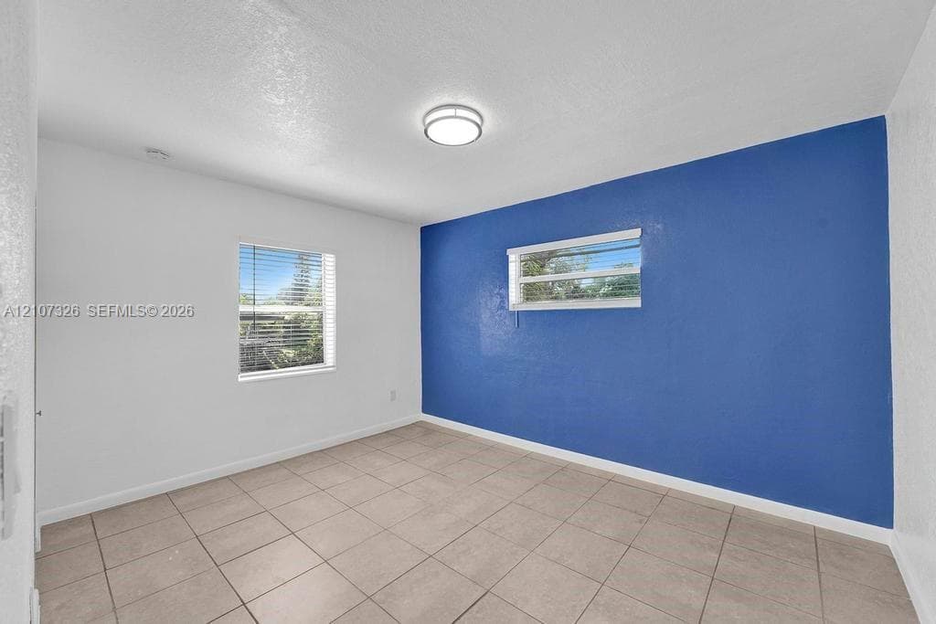 Interior room featuring neutral ceramic tile flooring, a prominent accent wall, two windows with horizontal blinds, and a flush-mount ceiling light fixture