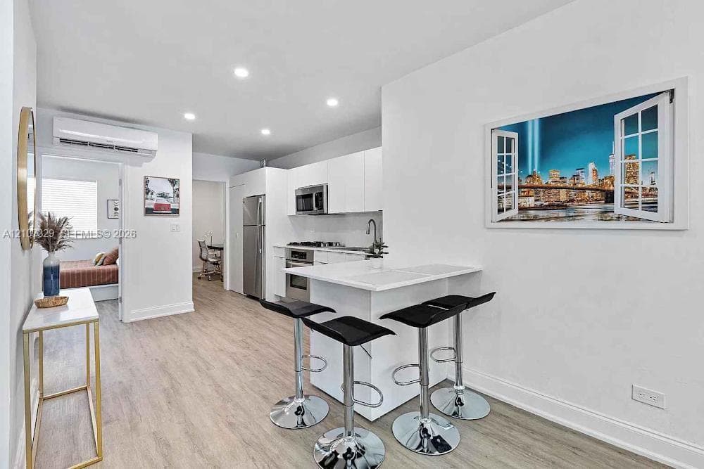 Kitchen featuring white flat-panel cabinetry, stainless steel appliances, a peninsula with stone-finish countertop, wood-finish flooring, and recessed lighting