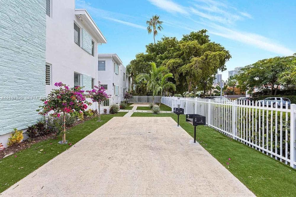 Outdoor walkway with green landscaping and a white fence.