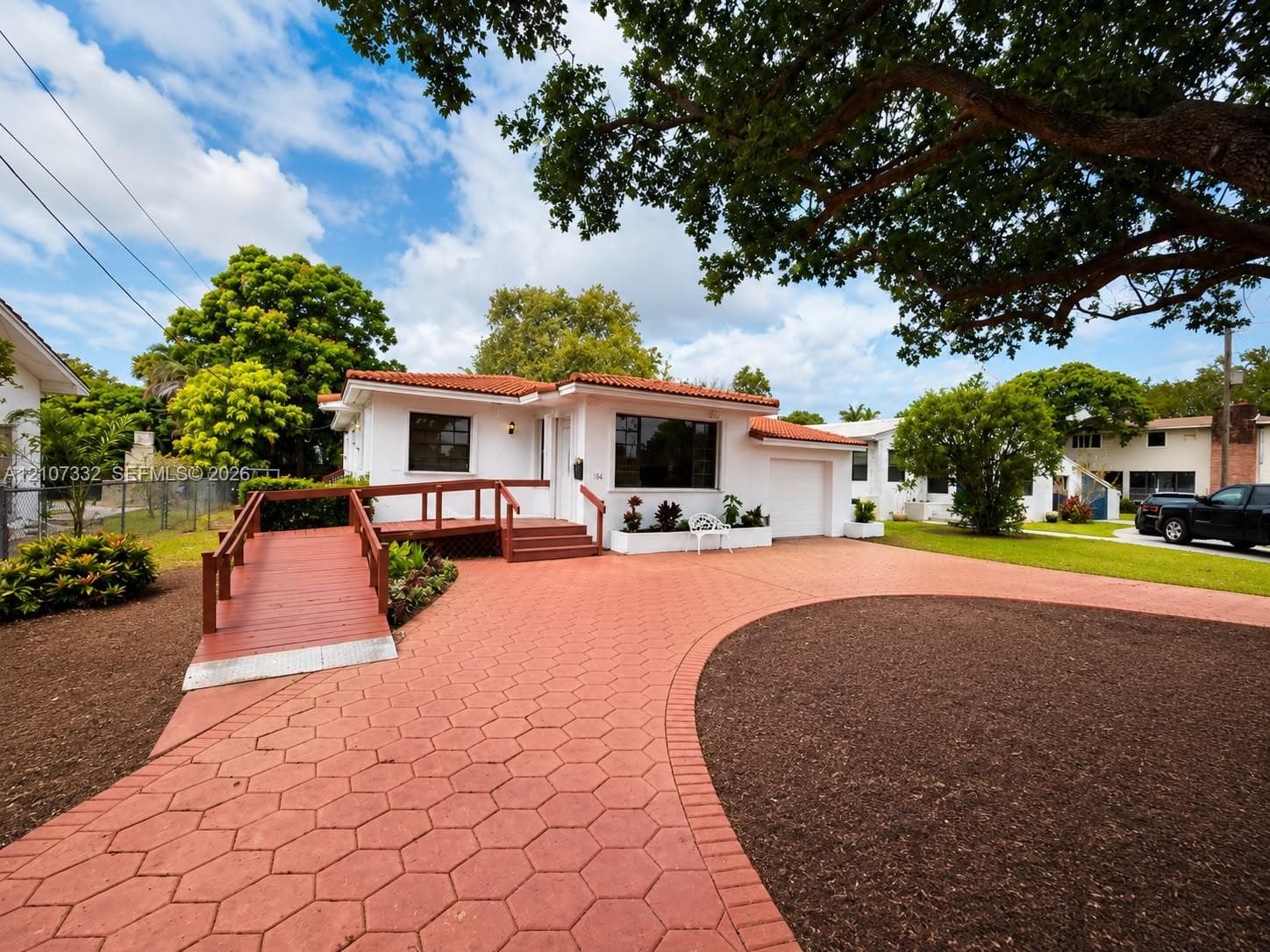 White stucco exterior featuring a red tile roof, patterned concrete paver driveway, attached garage, and wood-railed access ramp