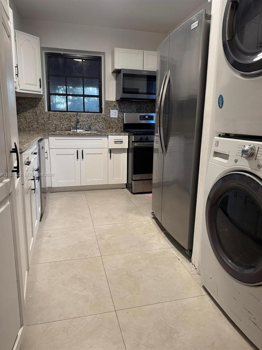 Kitchen featuring white shaker-style cabinetry, stone countertops, stainless steel appliances, and large-format tile flooring