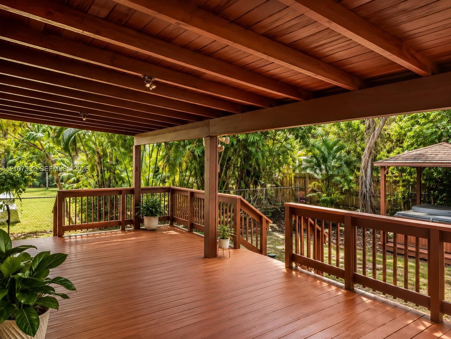 Covered wooden deck featuring exposed beam ceiling, built-in wooden railings, staircase access to the rear grounds, and an integrated gazebo structure