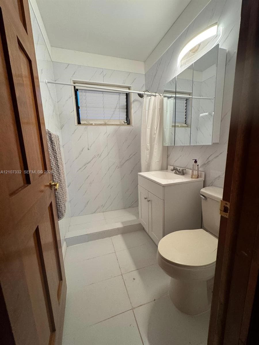 Full bathroom featuring a single-sink vanity with white cabinetry, a tri-fold medicine cabinet, white floor tiling, and wall surround with stone-pattern finish