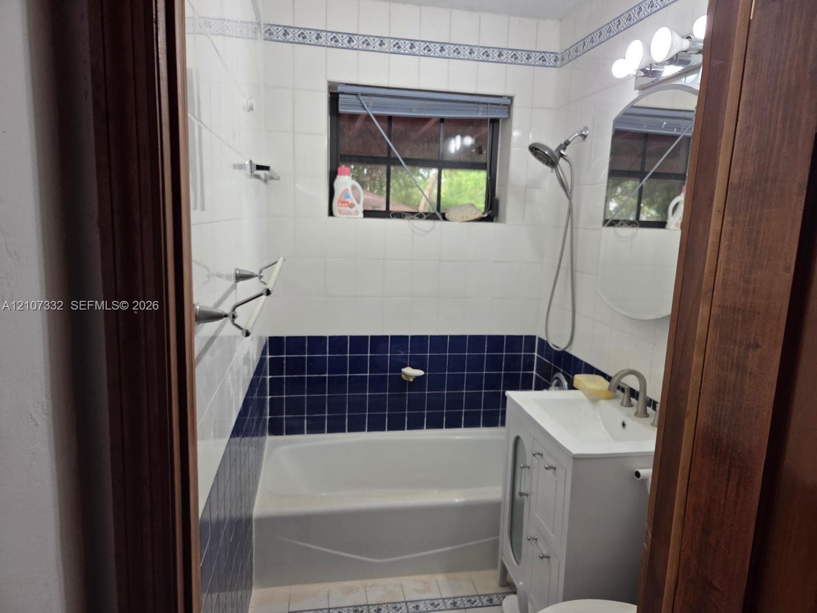 Full bathroom featuring white and deep blue wall tiling with decorative border, white vanity with integrated basin, silver-finish hardware, and a combination tub and shower