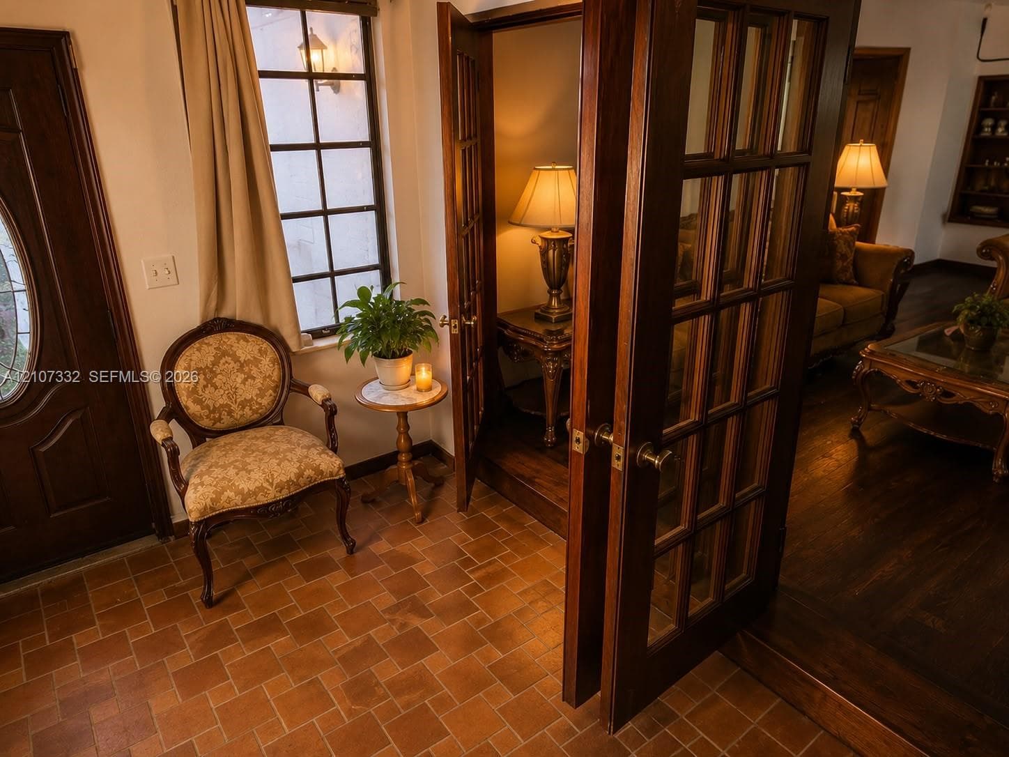 Entryway featuring terra-cotta tile flooring, multi-pane glass windows, and a solid wood door with an oval glass insert