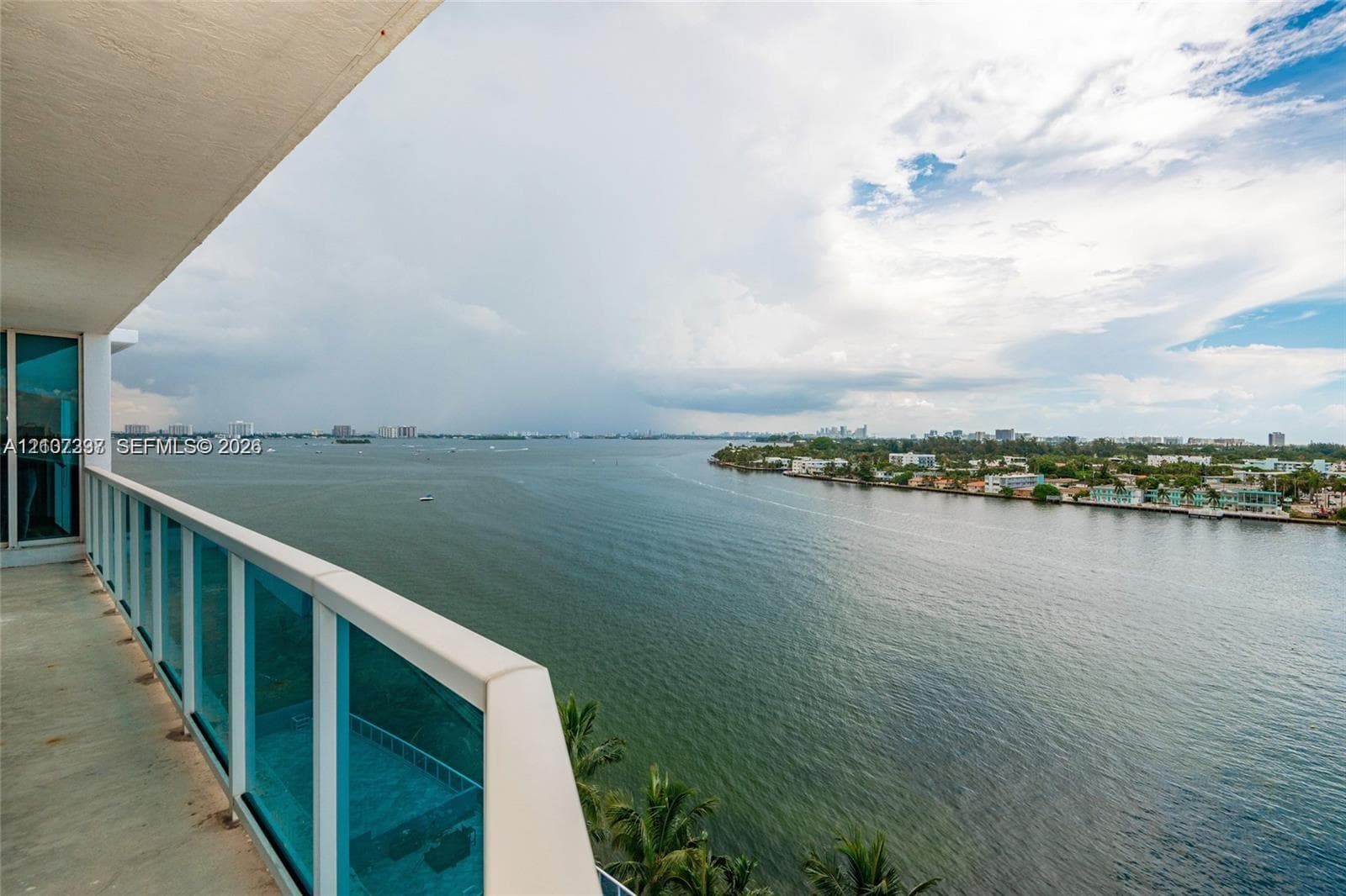 Covered balcony featuring concrete flooring and a glass-paneled railing with a metal frame, overlooking the water