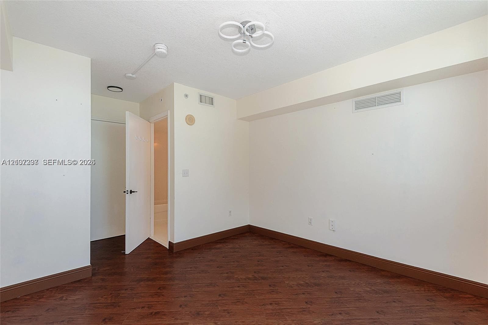 Interior space featuring wood-finish flooring, a contemporary multi-ring flush mount light fixture, and an open doorway