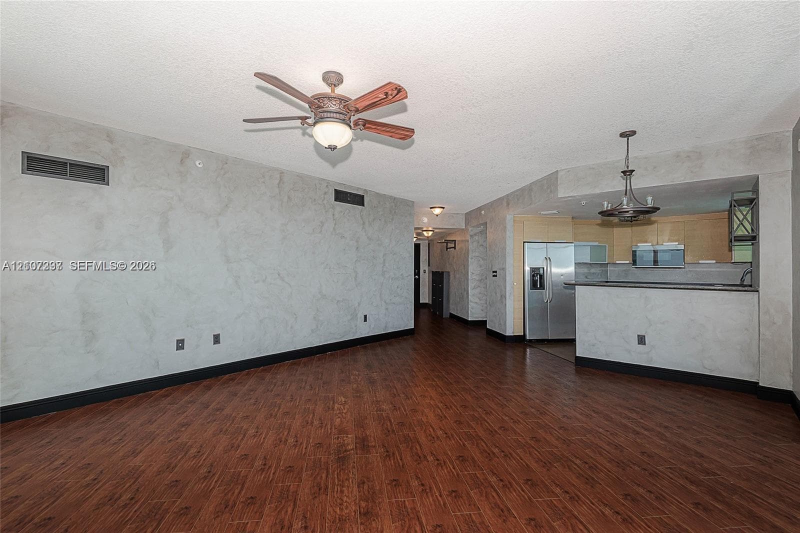 Living space featuring wood-finish flooring, custom textured wall finishes, a ceiling fan with integrated lighting, and a kitchen equipped with stainless steel appliances and a breakfast bar