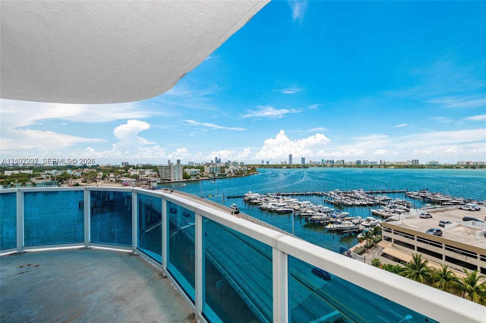 Private balcony featuring blue-tinted glass railings and concrete flooring, overlooking an expansive marina, open water, and coastal horizon