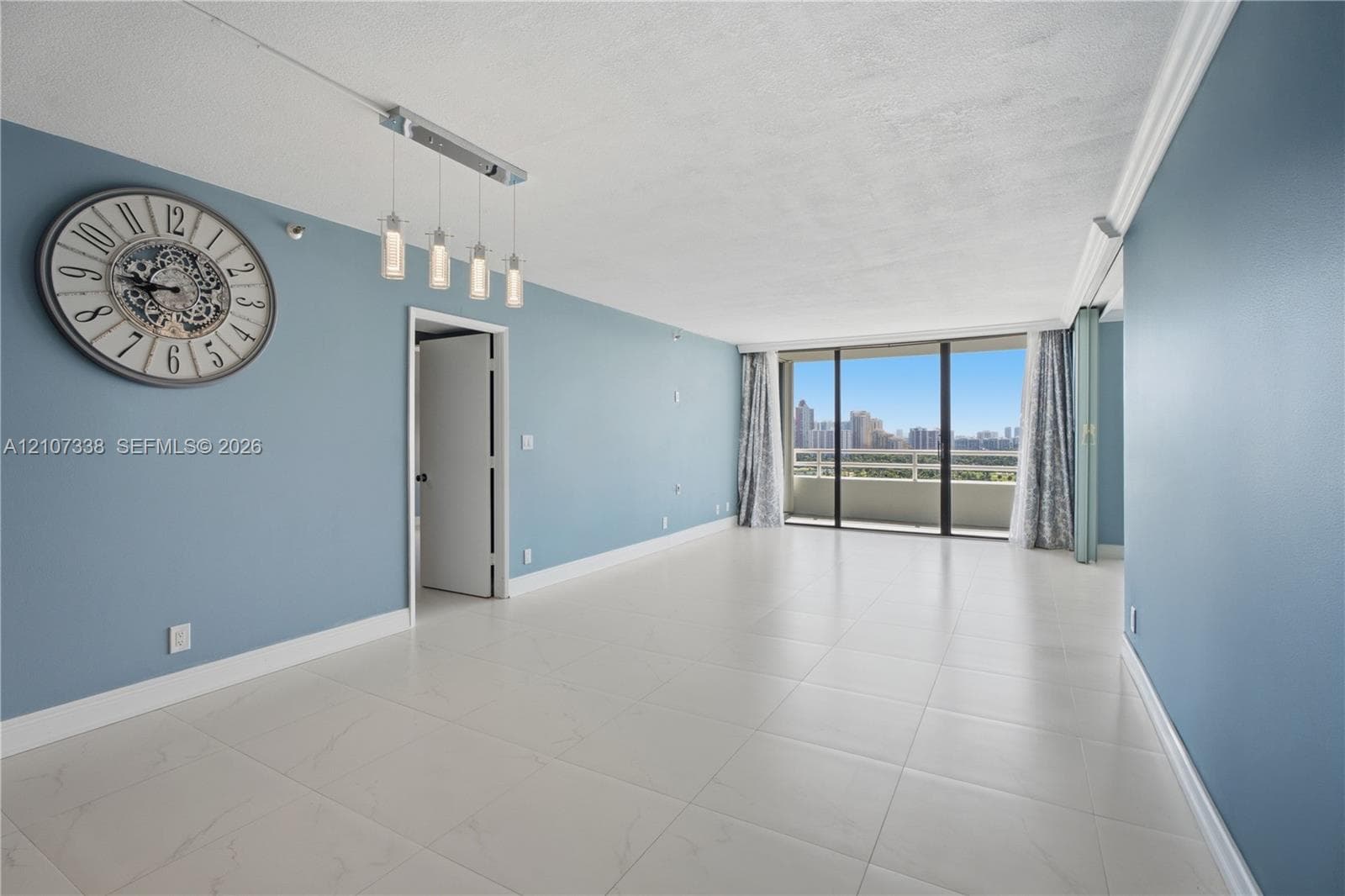 Open-concept living space featuring large-format tile flooring, floor-to-ceiling glass sliding doors, private balcony, and multi-light linear pendant fixture