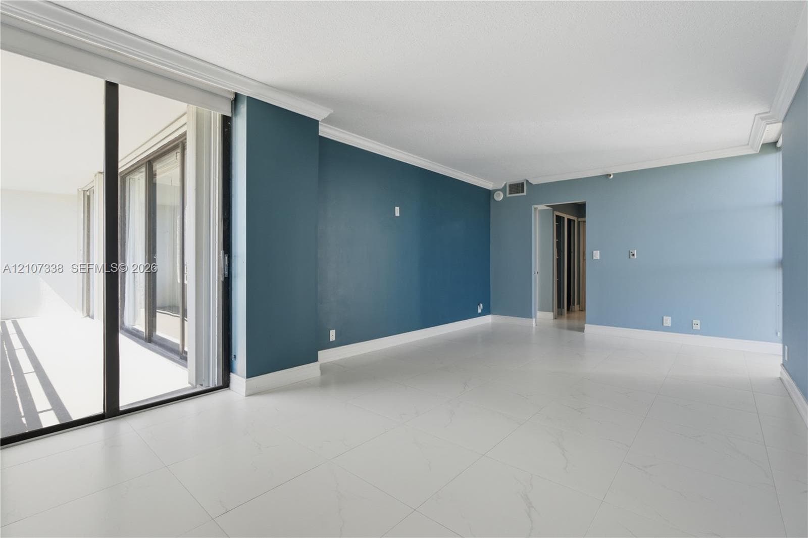 Large living area featuring polished tile flooring, floor-to-ceiling sliding glass doors, crown molding, and neutral wall tones