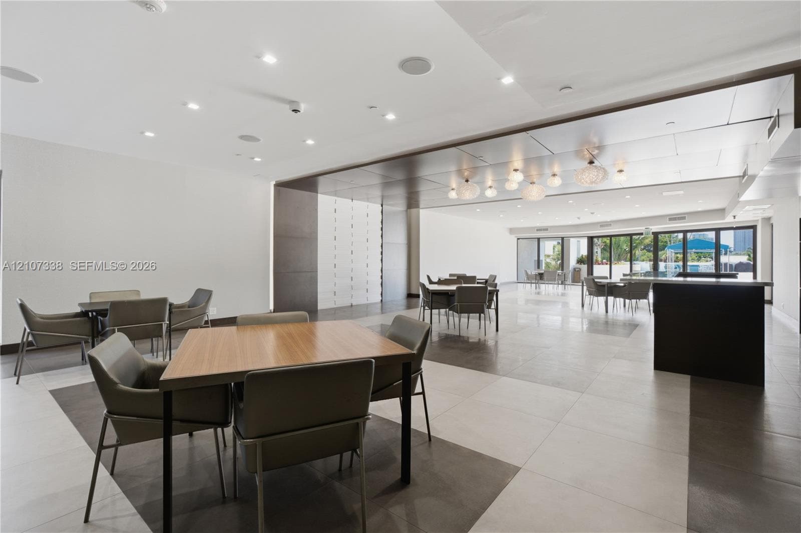 Spacious interior featuring large-format tile flooring, a dark-toned drop ceiling with integrated recessed lighting, decorative globe pendant lights, and floor-to-ceiling glass panel doors