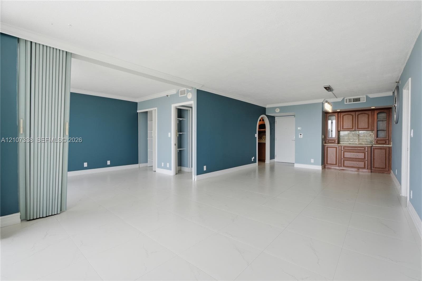 Open-concept living space featuring large-format tile flooring, built-in wooden cabinetry, an arched doorway, and a vertical sliding room partition