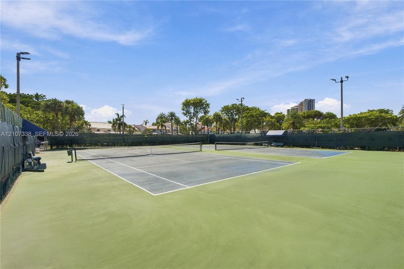 Dual hard-surface tennis courts featuring perimeter fencing, integrated court lighting, and netted boundaries