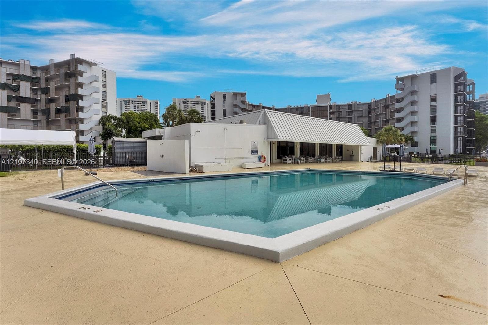 Multi-story residential building exterior featuring a covered entryway, paved surface parking, and curated landscaping