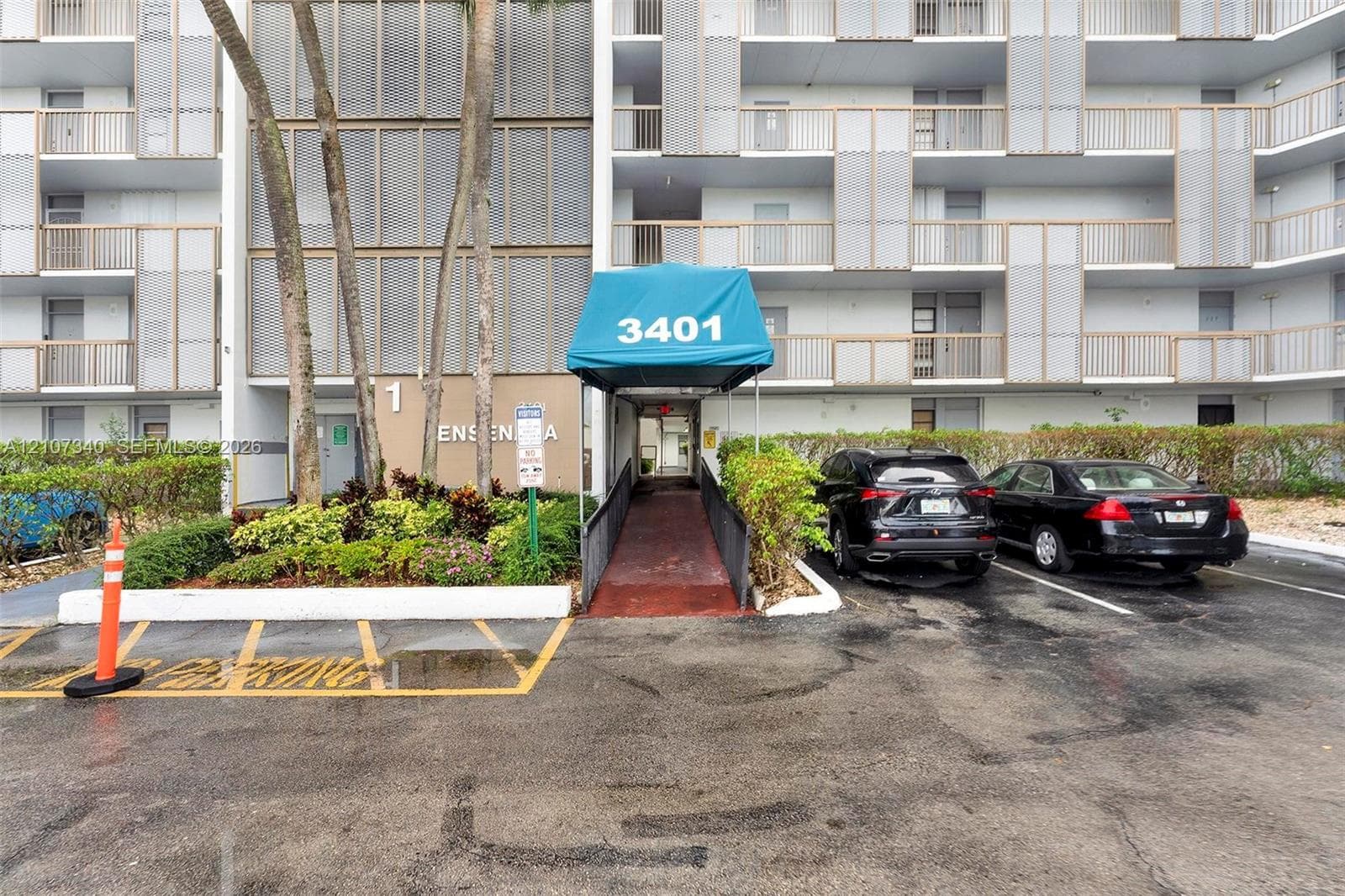 Multi-story residential building exterior featuring a covered entryway, paved surface parking, and curated landscaping