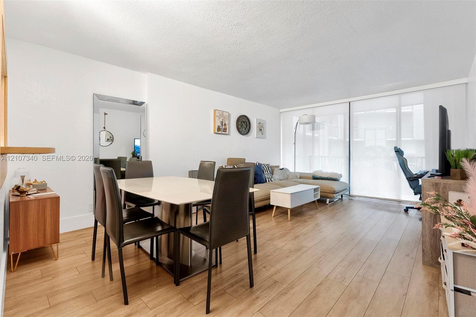 Open-concept living space featuring wood-finish flooring, a full-length wall mirror, and floor-to-ceiling sliding glass doors with roller shades