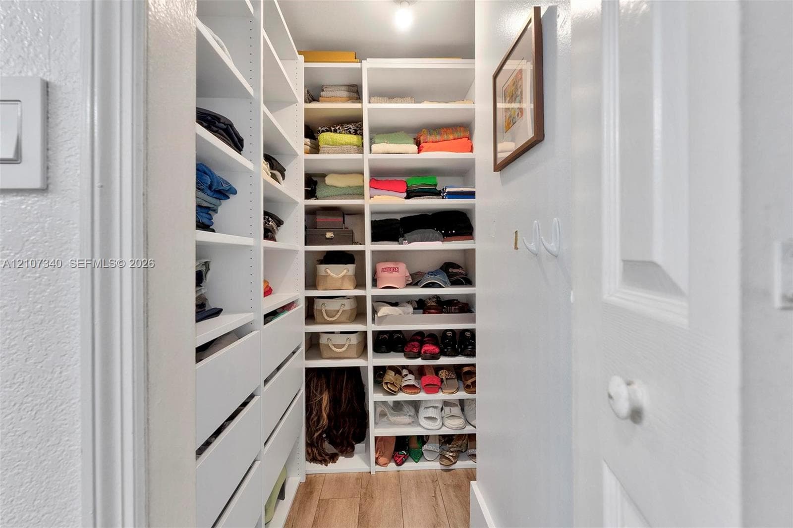 Walk-in closet featuring white built-in shelving, integrated storage drawers, and wood-finish flooring