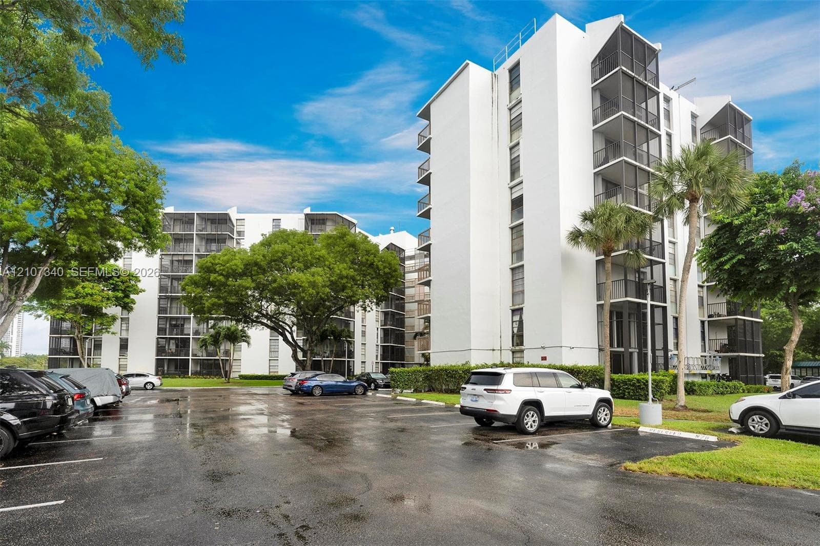 High-rise residential exterior featuring white stucco siding, screened balconies, and paved surface parking