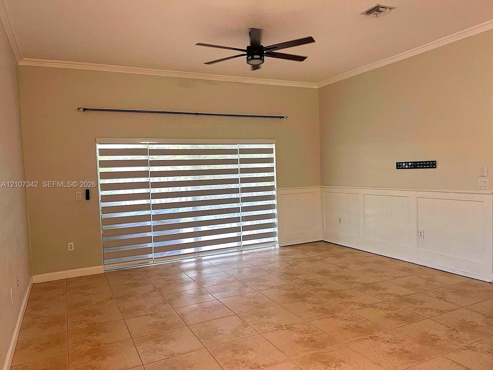 Spacious interior featuring large-format ceramic tile flooring, beadboard wainscoting, and a central ceiling fan