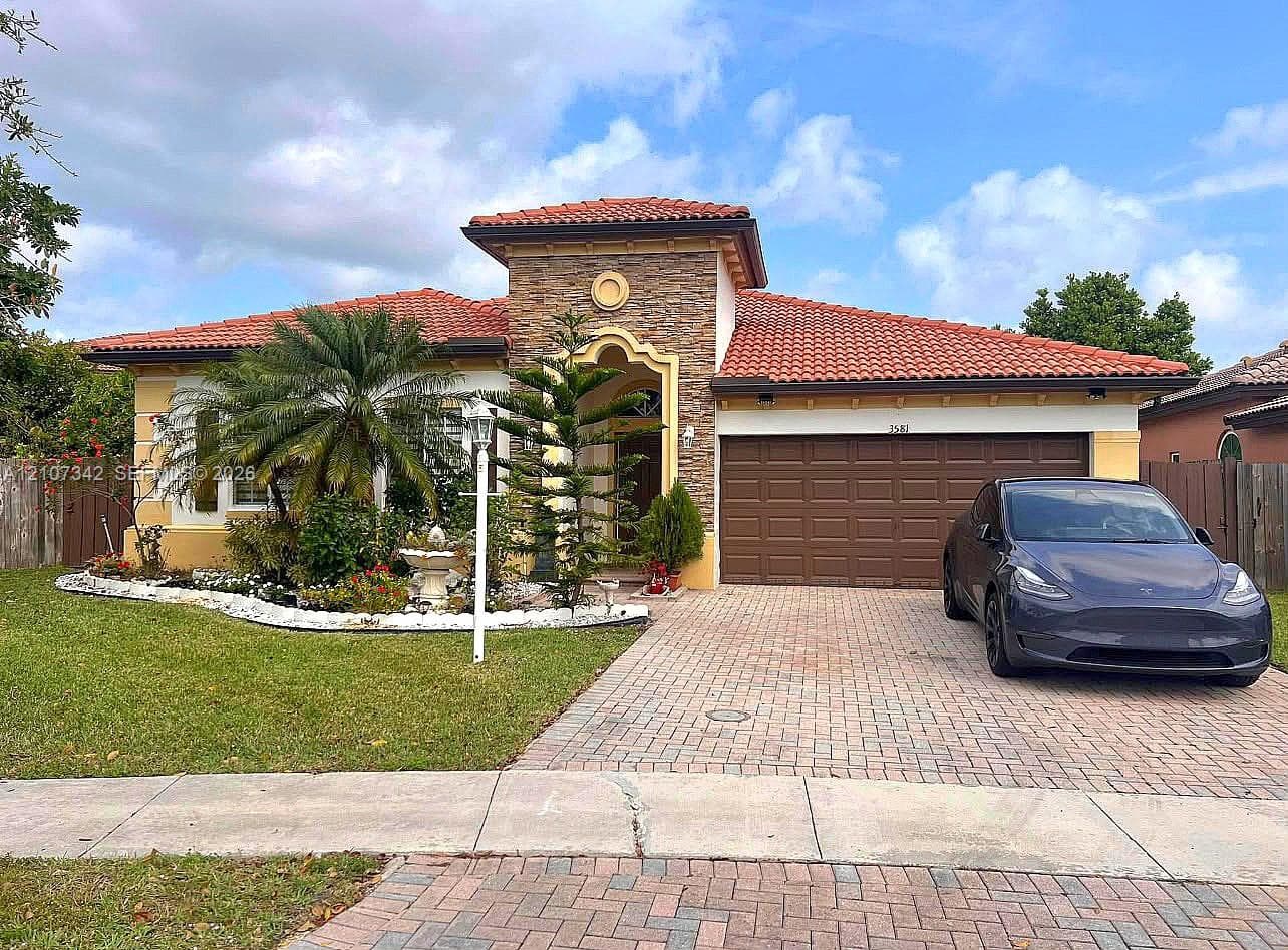 Single-story exterior featuring a stacked-stone facade, tile roof, arched entryway, and paver driveway