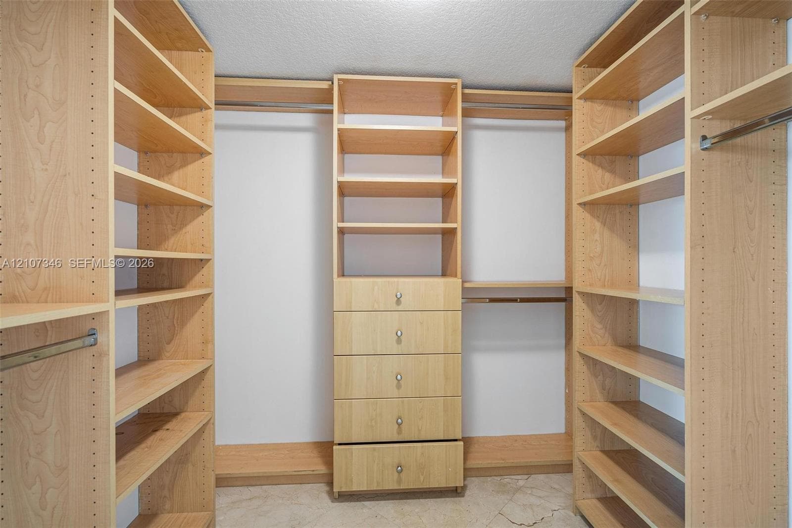 Custom-built closet featuring adjustable wood-finish shelving, integrated clothing rods, five-drawer cabinetry with metal pulls, and tile flooring