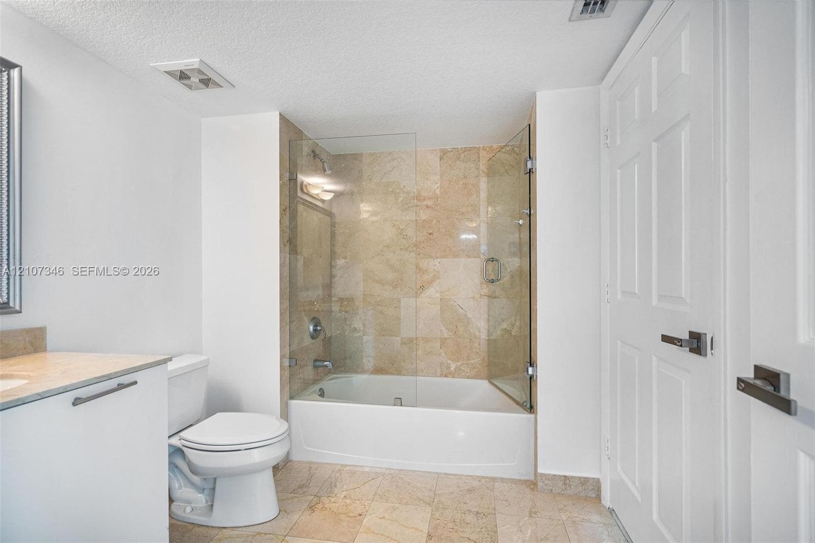 Bathroom featuring stone-tile flooring and wall surround, frameless glass shower enclosure, bathtub with integrated shower hardware, and a solid-surface vanity countertop
