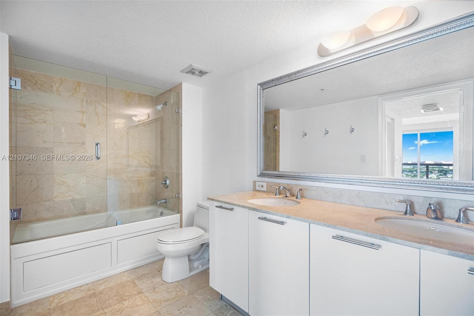 Bathroom featuring a dual-sink vanity with a stone countertop, a glass-enclosed tub shower with stone tile surround, and a large wall-mounted mirror