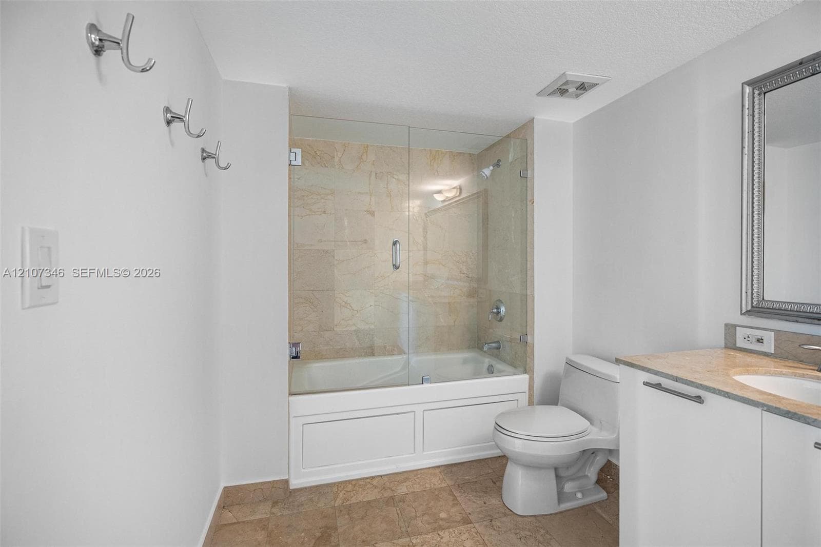 Full bathroom featuring a glass-enclosed tub with stone tile surround, stone-top vanity with an integrated sink, and tile flooring