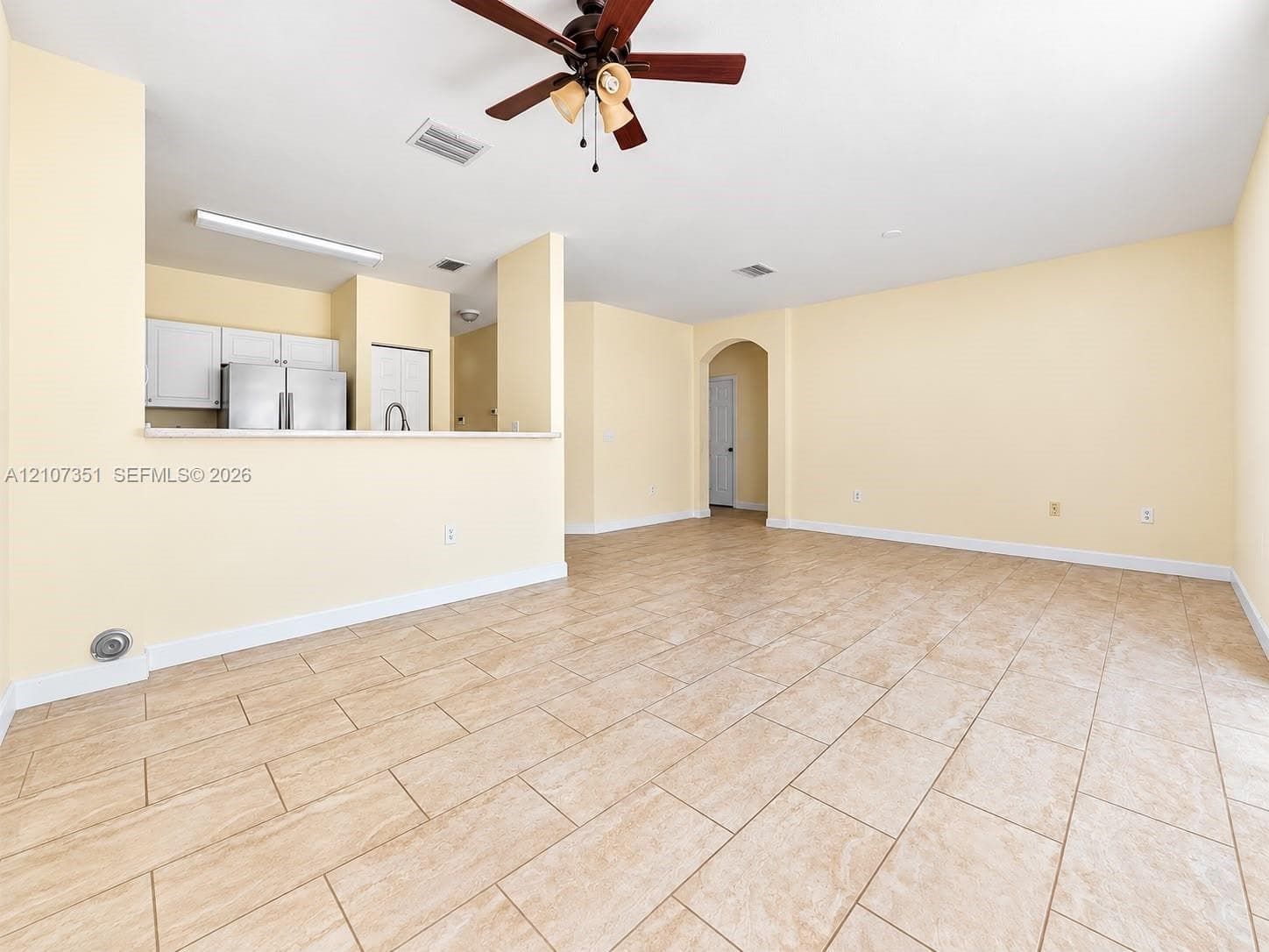 Open interior featuring ceramic tile flooring, a multi-blade ceiling fan with integrated lighting, and a breakfast bar overlooking white cabinetry