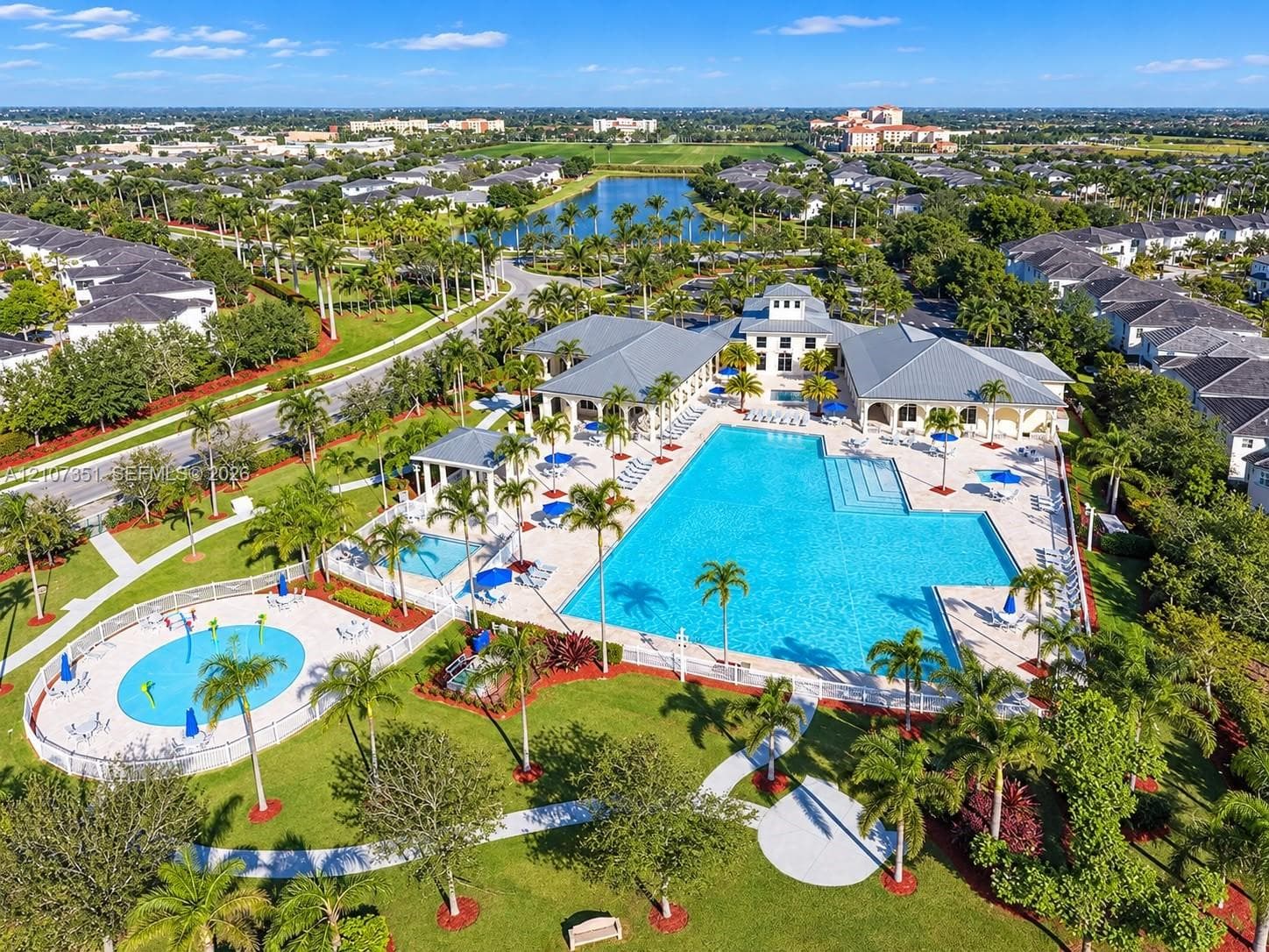 Community recreation center featuring an expansive swimming pool, separate splash pad, covered pavilion, and surrounding landscaped grounds