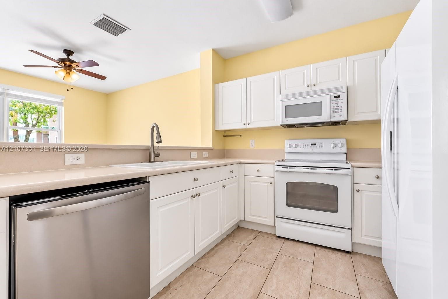 Kitchen featuring white cabinetry, solid-surface countertops, tile flooring, stainless steel dishwasher, and a ceiling fan
