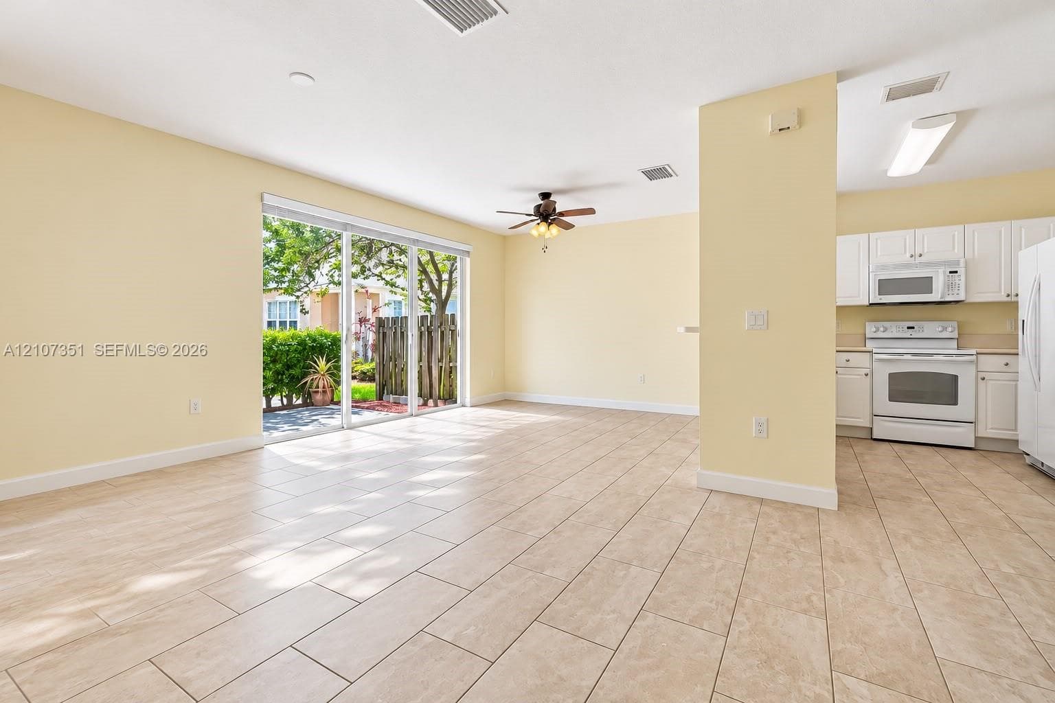 Neutral tile flooring, sliding glass door, ceiling fan, white kitchen cabinetry, and integrated white appliances