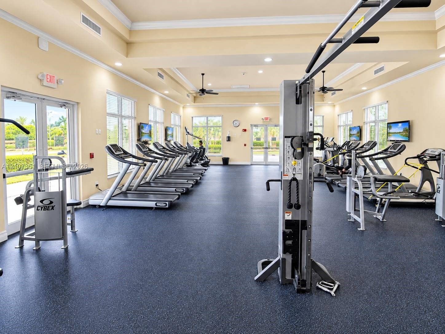Fitness center featuring rubberized flooring, recessed tray ceilings, multiple glass-paned double doors, and expansive windows