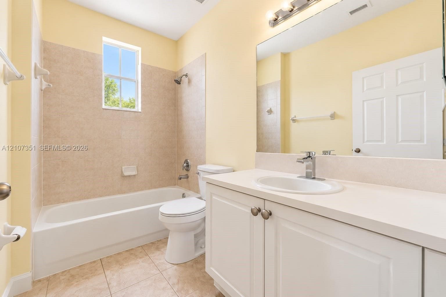 Bathroom featuring a white vanity cabinet with an integrated sink and chrome faucet, a large wall-mounted mirror, a tiled shower-tub combination, and ceramic tile flooring